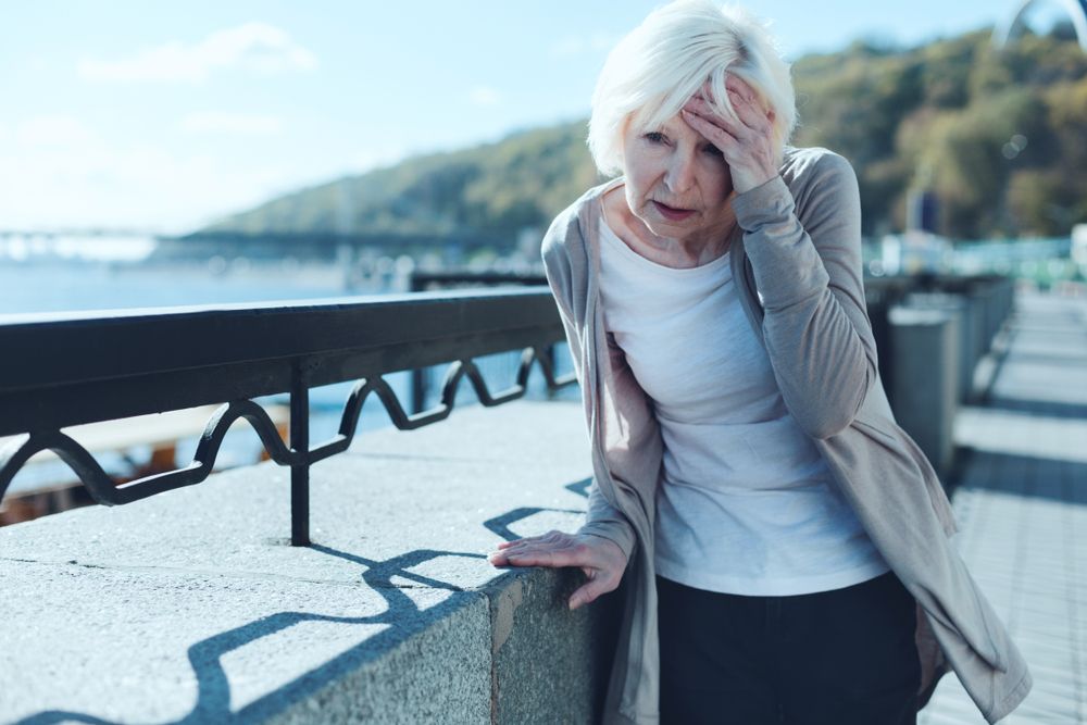 Older woman holding head in hands and leaning on railing
